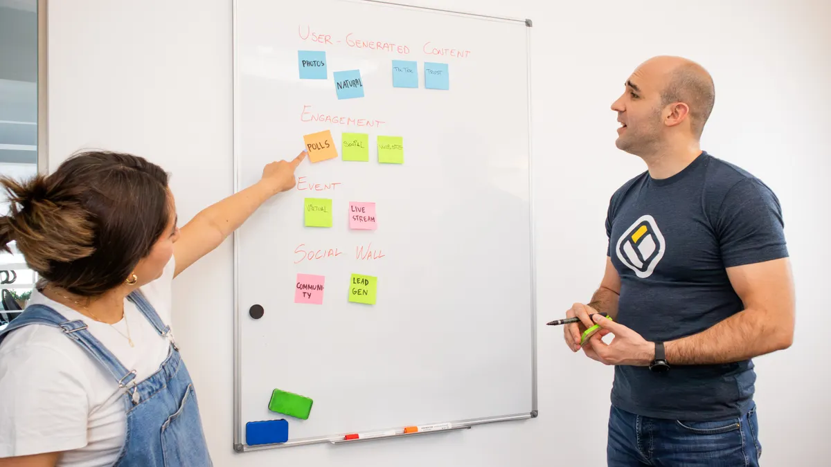 Two people organizing sticky notes on a whiteboard