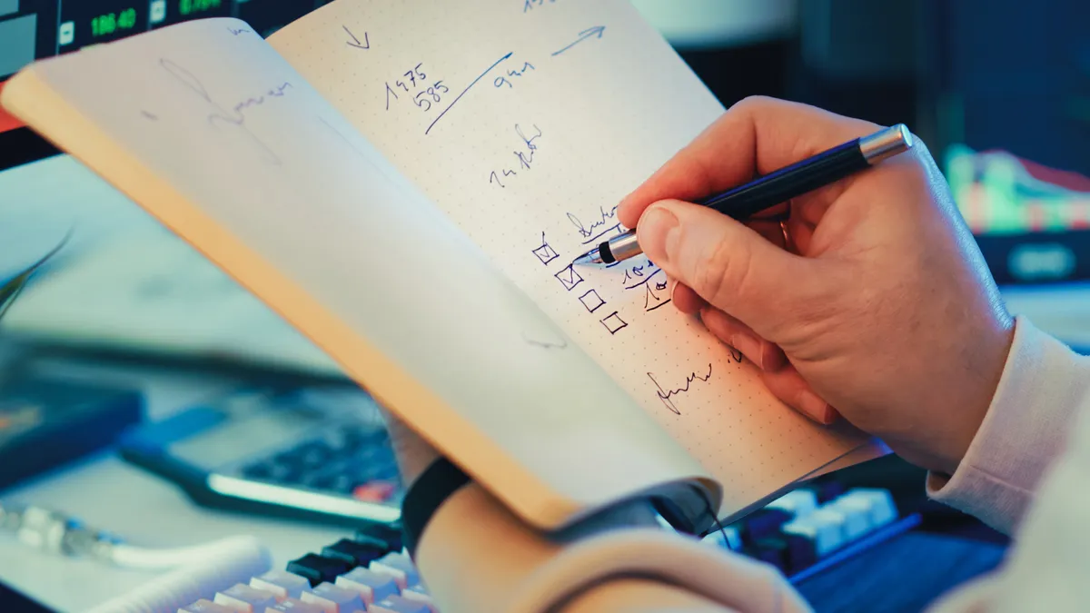 hand checking boxes in a notebook beside a keyboard