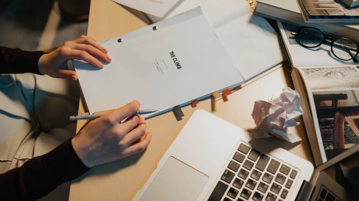 Hands reviewing a document over a laptop on a cluttered desk